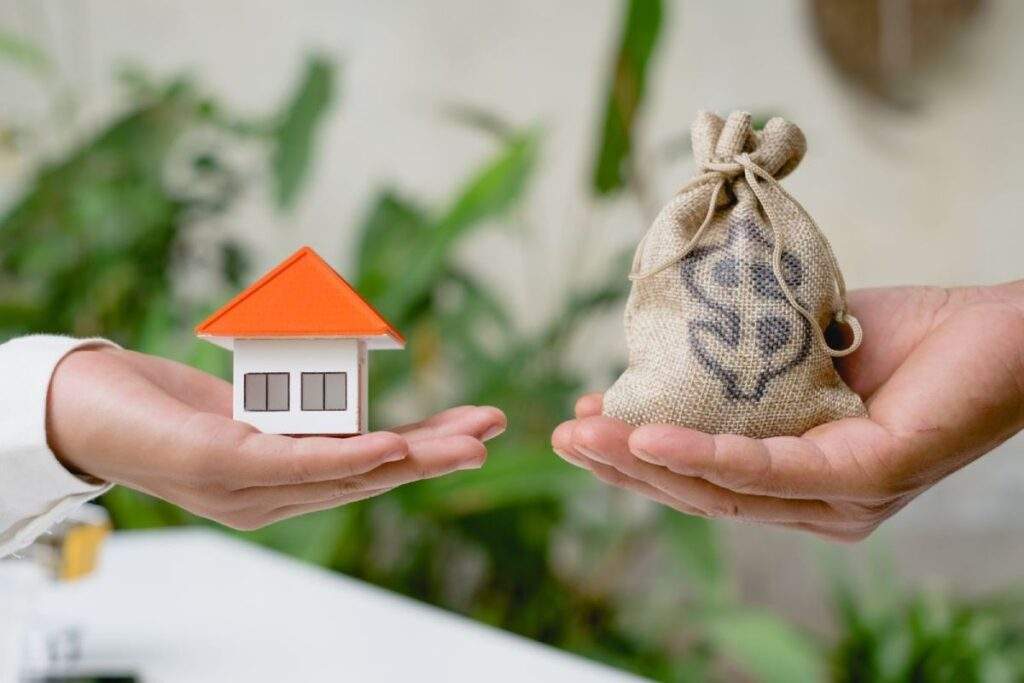 Hand holding small house model and hand holding money bag, symbolizing Texas real estate investment returns under OBBB policy changes.