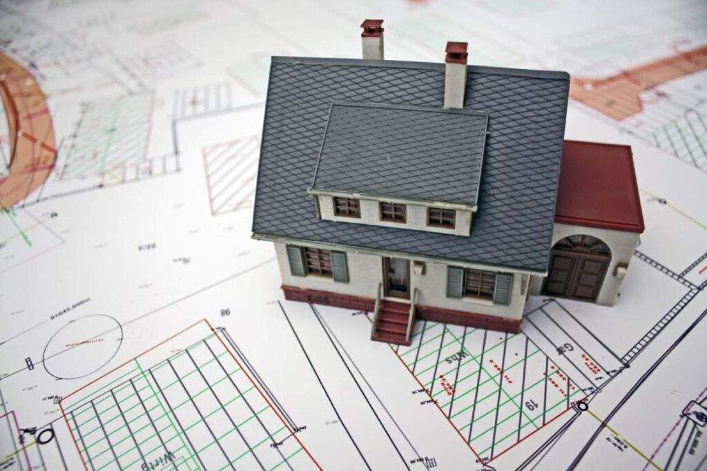 Model house placed on architectural blueprints representing before and after OBBB real estate investment analysis in Texas.