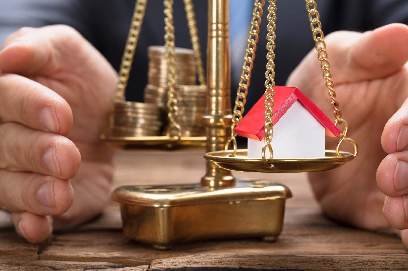 Businessman balancing a model home against gold coins on a scale, illustrating residential real estate as an inflation hedge